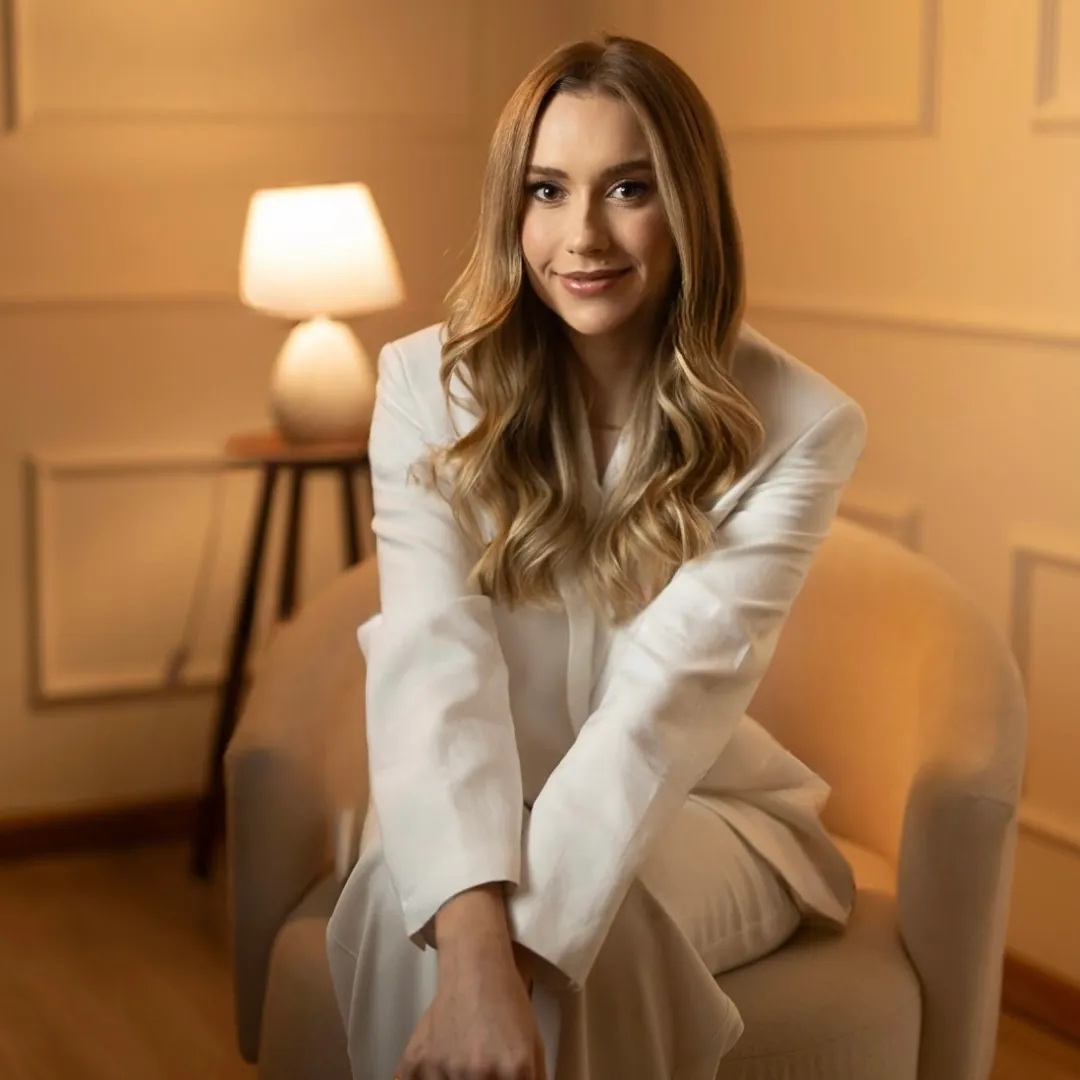 Dra. Amanda Prado em ambiente de consultório, sentada em poltrona clara
